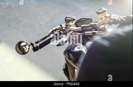 Close up of handsome biker sitting on motorcycle and reflecting in side view mirror. Stock Photo