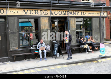 People sitting outside Verde & Company drinking tea and eating at a table in summer in Spitalfields East London England E1 UK  KATHY DEWITT Stock Photo