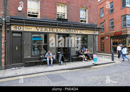 People sitting outside Verde & Company drinking tea and eating at a table in summer in Spitalfields East London England E1 UK  KATHY DEWITT Stock Photo
