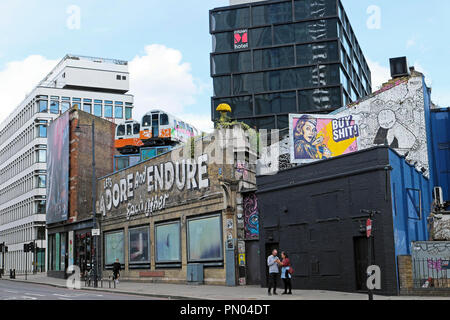 'Let's Adore and Endure Each Other' graffiti on wall with train carriages on roof Great Eastern Street art in Shoreditch East London UK  KATHY DEWITT Stock Photo