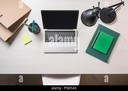 top view of workplace with folders, note and laptop with blank screen on table Stock Photo