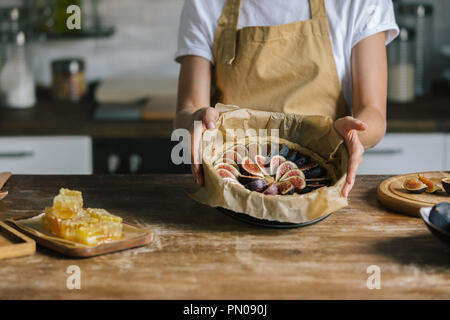 cropped shot of woman holding baking form with sliced figs over rustic wooden table Stock Photo