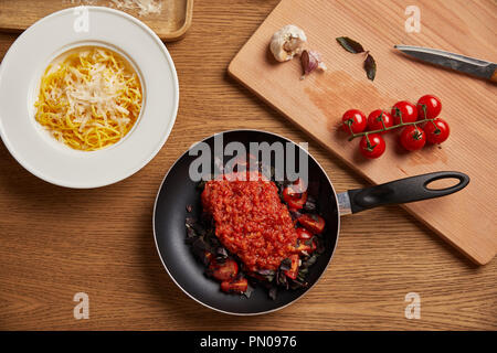 top view of plate of spaghetti and tomato sauce in frying pan on wooden table Stock Photo