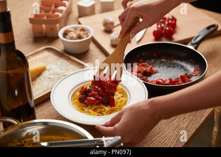 cropped shot of woman putting tomatoes from frying pan onto spaghetti in plate Stock Photo