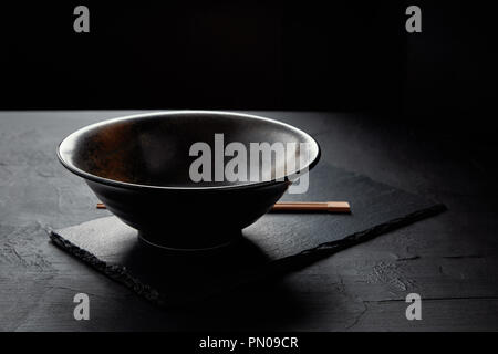 close-up view of empty bowl and chopsticks on black slate board Stock Photo