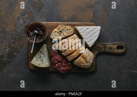 top view of sliced bread, delicious cheese, salami and jam on wooden cutting board Stock Photo