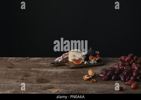 fresh ripe grapes, nuts and delicious cheese on wooden table on black Stock Photo