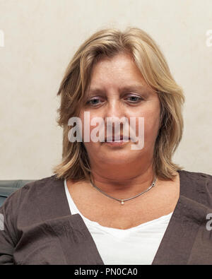 Portrait of mature 59 year old woman with neutral expression at home on sofa looking down Stock Photo