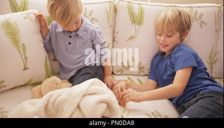 Young blond boy tickling his brother's feet on a sofa. Stock Photo