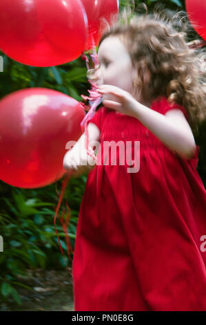 A young girl in a red dress holding balloons.