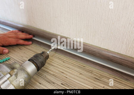 The man secures the baseboard to the wall Stock Photo