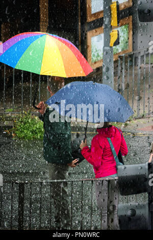 Looking through a raindrop covered window at people caught in heavy autumn rain shower with their umbrellas up. Stock Photo