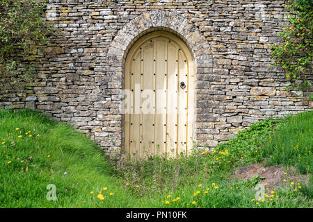 Arched wooden Garden door and cotswold stone wall in front of a house in the cotswold village of Calmsden, Cotswolds, Gloucestershire, England Stock Photo