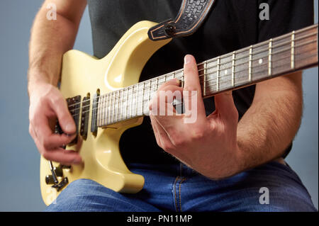 A man in a black shirt and jeans playing an electric guitar. Fingers detail, blue background. Stock Photo