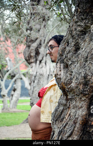 Pregnant woman hiding her face from behind a tree and boyfriend taking off her face, funny photo of pregnant, joke Stock Photo