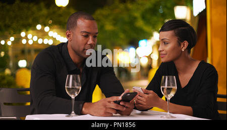 Casual African-American couple talk while using smartphones on date Stock Photo