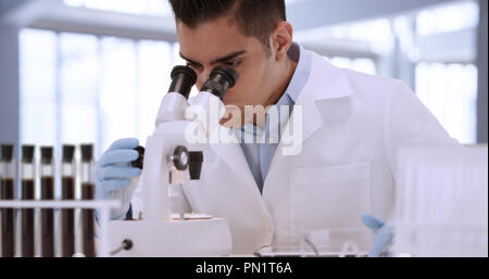 Young Hispanic male scientist in laboratory looking through microscope Stock Photo