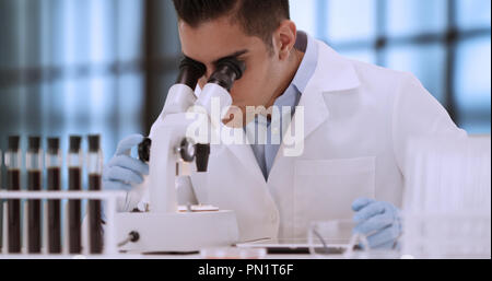 Young Hispanic forensic scientist looking at blood sample through microscope Stock Photo