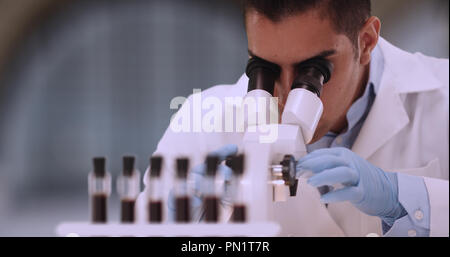 Hispanic male forensic scientist examining blood sample through microscope Stock Photo