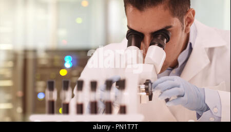 Millennial Hispanic medical research scientist in lab using microscope Stock Photo