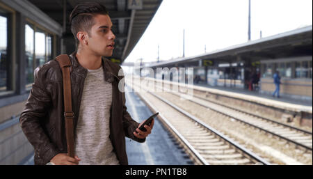 Handsome millennial Latin male at the train station hailing a ride Stock Photo