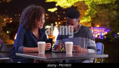 Black male and female meeting for coffee at night use tablet computer Stock Photo