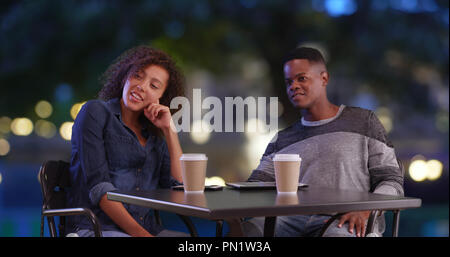Black male and female enjoy evening outdoors drinking coffee and talking Stock Photo