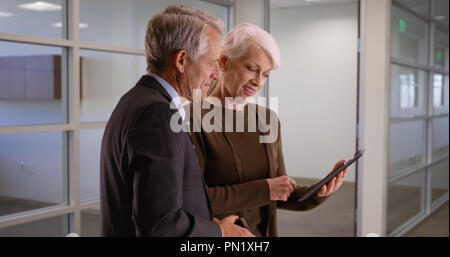 Senior business team going over financial data on tablet in the hallway Stock Photo