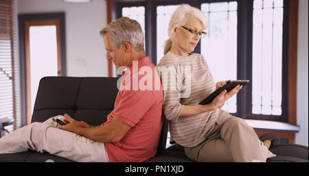 Senior couple using devices on couch at home Stock Photo