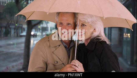 Smiling mature couple standing under umbrella Stock Photo