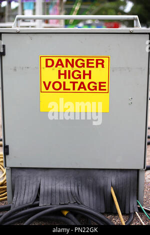A metal electric power supply junction cabinet box at a carnival has a yellow and red danger high voltage sign on it. Stock Photo