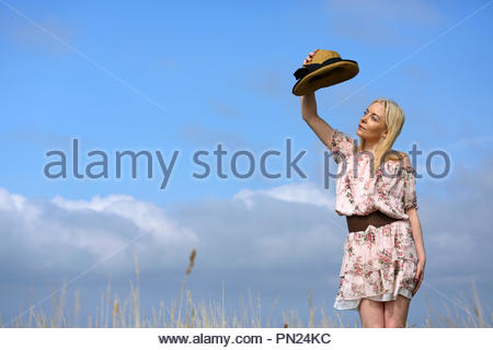 Blonde woman in a summer dress putting on a straw hat Stock Photo