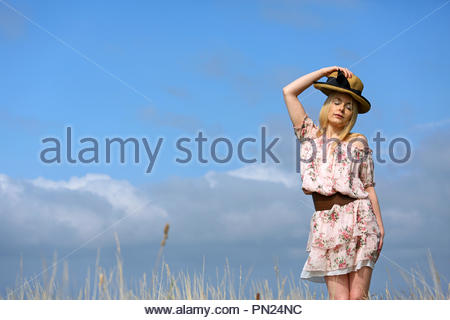 Blonde woman in a summer dress putting on a straw hat Stock Photo