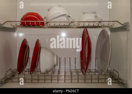 White porcelain dishes dried on metal dish rack. Way to organize kitchen and minimize space with modern drainer in cabinet against white background. Stock Photo