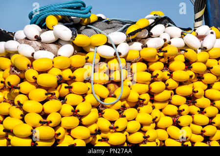 Yellow floats on the pile, covering fishing nets on the blue boat in the summer sun, close up. Fishing floats with rope knot netting piled. Stock Photo