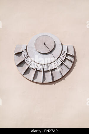 Old solar clock on a white wall, close up. Old fashioned sun dial on a stone wall isolated on white, detail of an old solar time marker. Sundial. Stock Photo