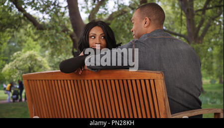 Youthful black couple flirtatiously stare at each other on public park bench Stock Photo