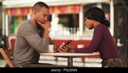 Black couple drinking coffee and browsing internet on smartphones on date Stock Photo