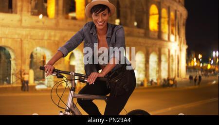 Smiling African millennial woman poses on bicycle near Roman Colosseum Stock Photo