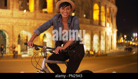 Smiling African millennial woman poses on bicycle near Roman Colosseum Stock Photo