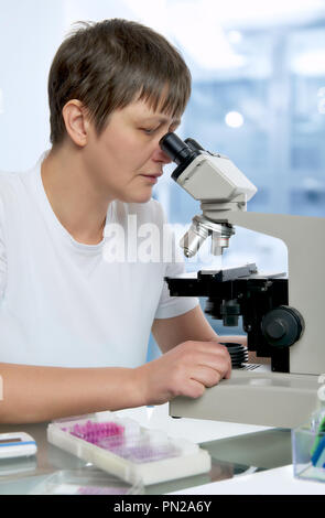 Senior female microscopist in modern laboratory looks in the microscope analyzing tissue samples Stock Photo