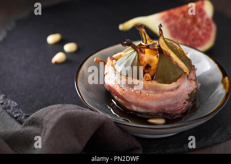 Closeup on baked fig stuffed with pine seeds and honey, wrapped in bacon on dark stone plate Stock Photo