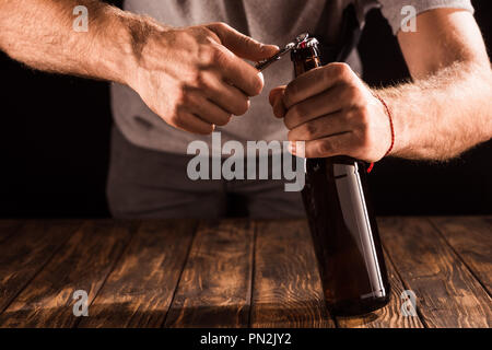 partial view of man opening beer bottle by opener at wooden table Stock Photo