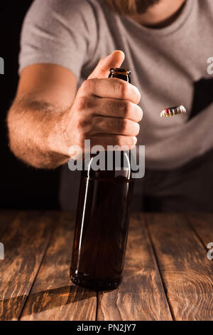 partial view of man opening beer bottle at wooden table Stock Photo