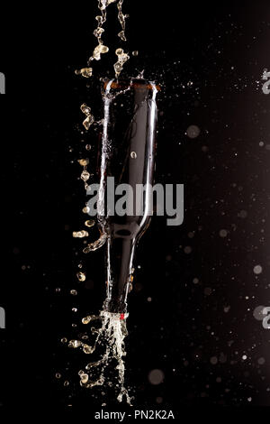 selective focus of beer pouring on bottle upside down with splashes around isolated on black background Stock Photo