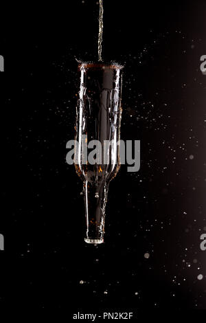 selective focus of beer pouring on bottle upside down with splashes around isolated on black background Stock Photo