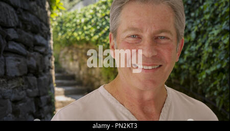 Happy mature Caucasian man smiles outside near stone staircase Stock Photo