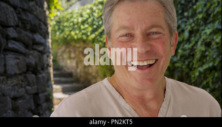 Happy mature Caucasian man smiles outside near stone staircase Stock Photo