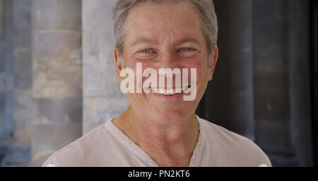 Old Caucasian male smiles happily near stone pillars Stock Photo
