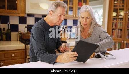 Charming mature white couple looking at handheld tech while eating lunch Stock Photo